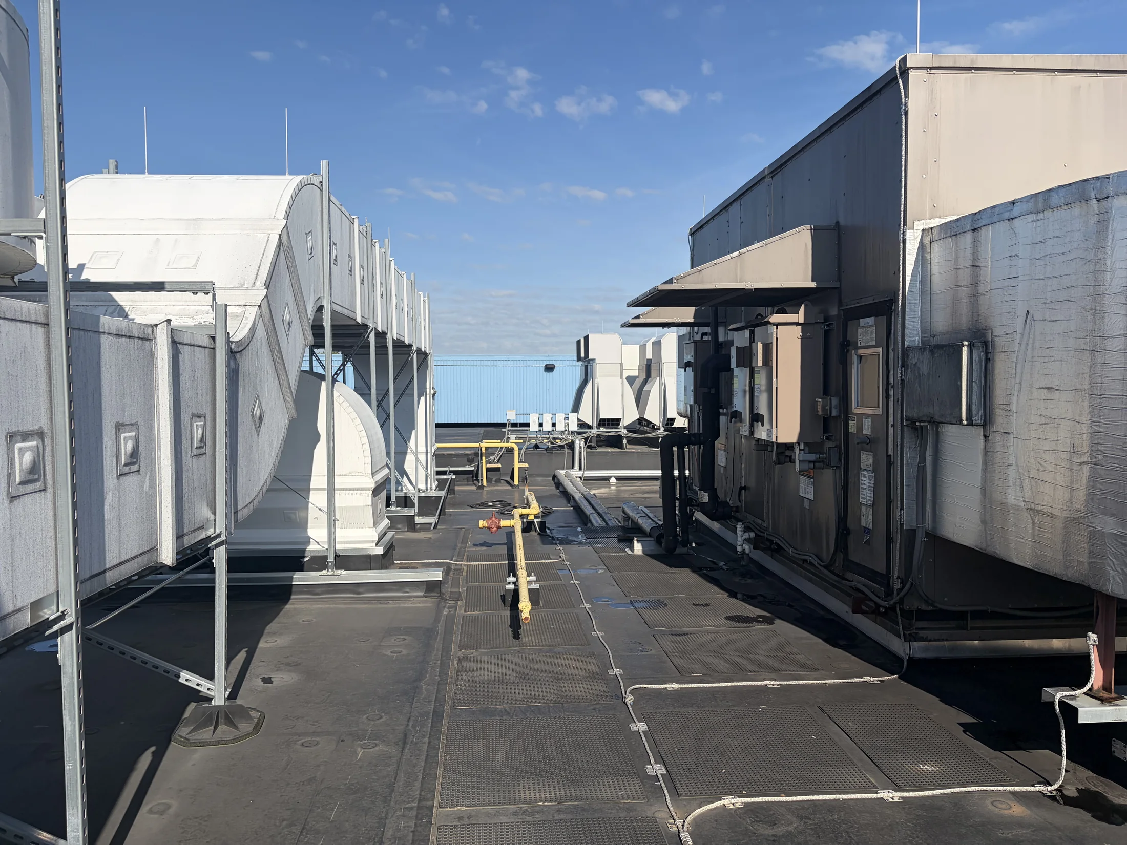 Long rooftop mechanical corridor lined with commercial air-handling equipment at a ZMS work site